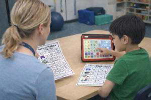 autistic boy with AAC device talking about preferences with occupational therapist