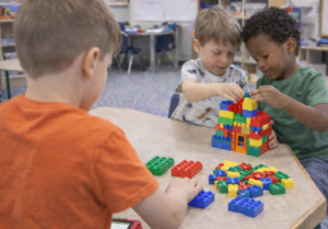 3 boys playing with duplo blocks at a table in a classroom